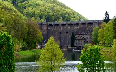 Der Diemelsee und seine Staumauer im Frühling umringt von Bäumen, deren Blätter verschiedenste Grüntöne haben.
